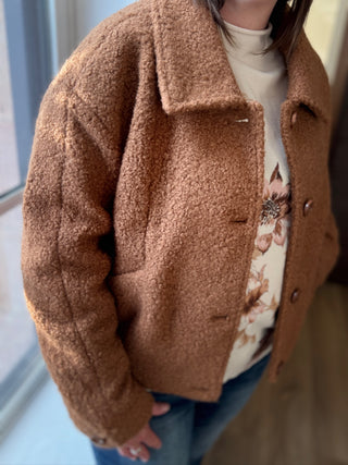 Person wearing a brown teddy coat with a blurred background