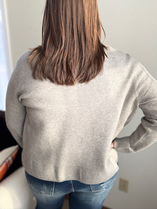 Person wearing a gray sweater and blue jeans with a neutral background