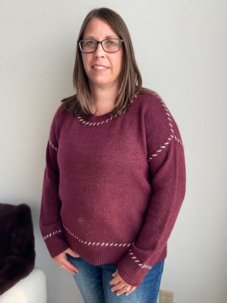 Woman wearing a maroon sweater with white patterns against a plain background