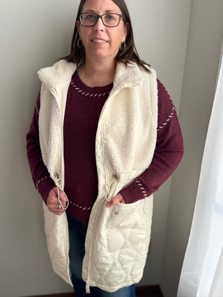 Woman wearing a white quilted vest over a red sweater against a neutral background