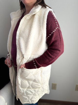 Person wearing a white quilted vest over a maroon long-sleeve shirt against a plain background