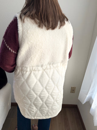 Person wearing a white quilted vest indoors against a plain wall.