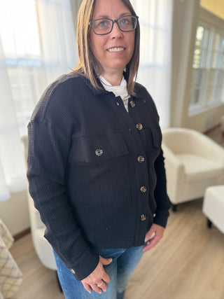 Woman wearing a black jacket with gold buttons in a room with white curtains and furniture.