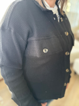 Person wearing a dark blue textured jacket with gold buttons indoors.