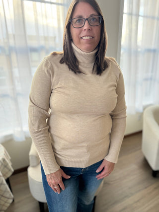 Woman wearing a beige sweater and blue jeans indoors.