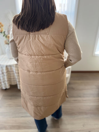 Person wearing a beige puffer vest in a room with a table and chair.