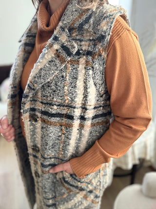 Person wearing a patterned vest over a brown sweater with a blurred background