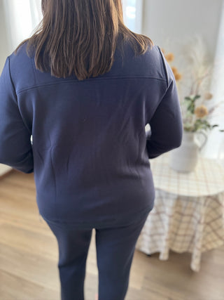 Person wearing a navy blue outfit in a room with a table and flowers.