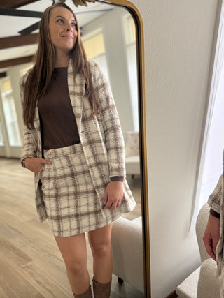 Woman wearing a plaid blazer and skirt standing in front of a mirror.