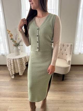 Woman wearing a green dress standing in a room with wooden floor and white furniture.