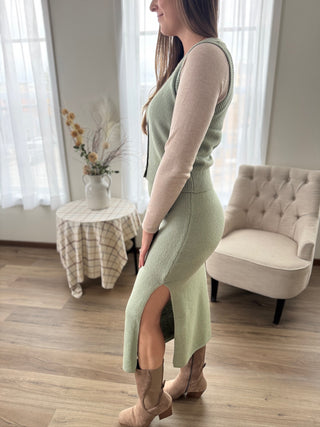 Woman in a green dress with a beige cardigan standing in a living room.