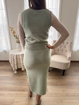 Person wearing a green knit dress in a room with curtains and furniture.