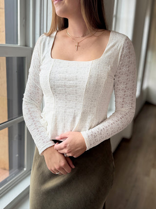 Woman wearing a white long-sleeve top and brown skirt indoors.
