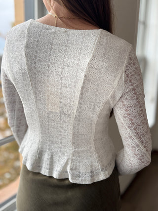 Woman wearing a light gray blouse with lace sleeves indoors.