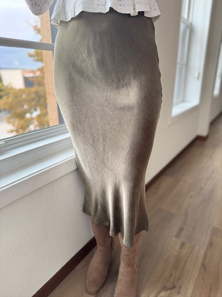 Person wearing a suede silver skirt standing by a window with a view of trees.