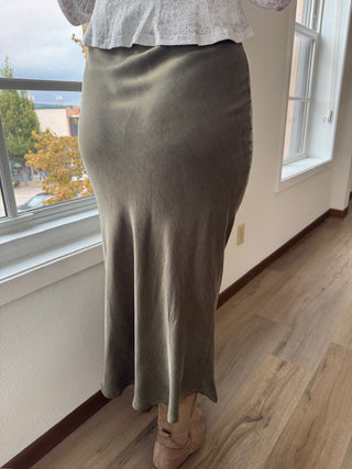 Person wearing a green skirt standing in a room with a window in the background