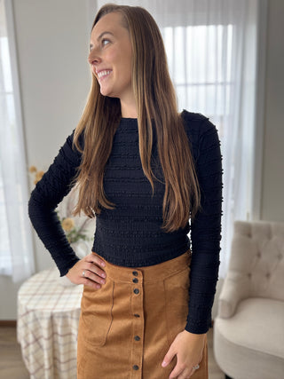 Woman wearing a black sweater and brown skirt indoors