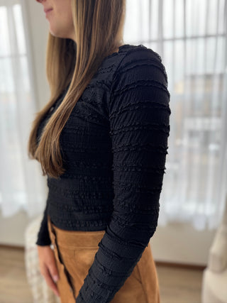 Person wearing a black textured long-sleeve top with blurred background