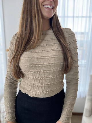 Woman wearing a textured beige long-sleeve top in a bright room.