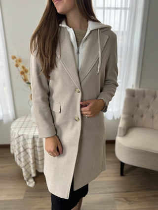 Woman wearing a beige hooded coat in a room with furniture.
