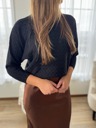 Person wearing a dark sweater and brown skirt indoors