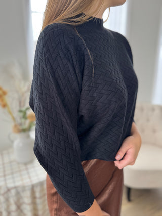 Person wearing a dark blue cable knit sweater in an indoor setting