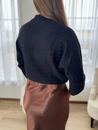 Person wearing a dark blue textured sweater and brown skirt indoors.