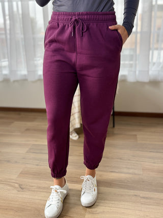 Person wearing purple jogger pants and white sneakers on a wooden floor.