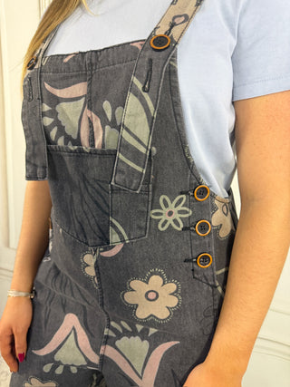 Person wearing floral-patterned denim overalls with a plain background
