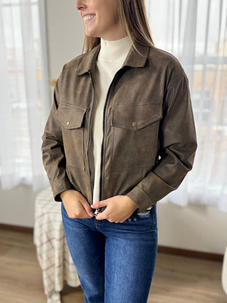 Woman wearing a brown jacket and blue jeans indoors