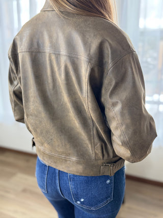 Person wearing a brown leather jacket and blue jeans indoors.