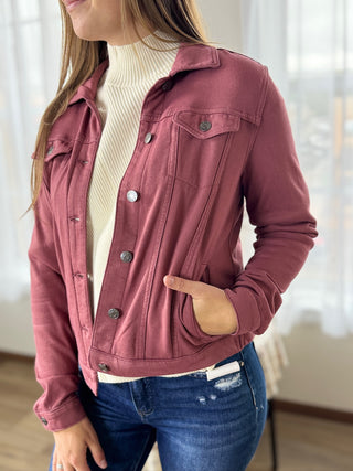 Person wearing a maroon jacket over a white turtleneck and blue jeans indoors.