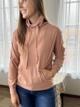 Woman wearing a pink hoodie in a room with light streaming through windows.