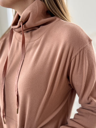 Close-up of a person wearing a ribbed brown sweater with a blurred background