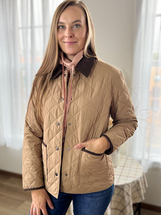 Woman wearing a beige quilted jacket indoors with a blurred background
