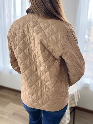 Person wearing a beige quilted jacket indoors with a neutral background