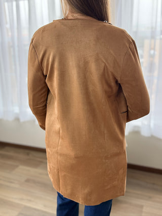 Person wearing a brown coat standing in a room with white curtains.
