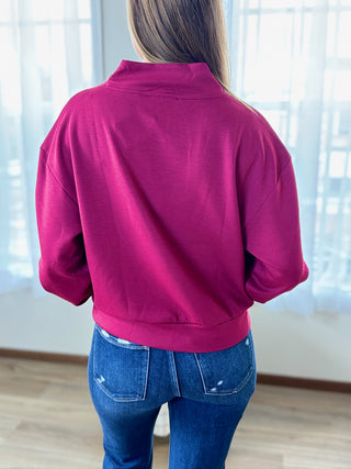 Person wearing a magenta jacket and blue jeans in a room with light-colored walls and floor.