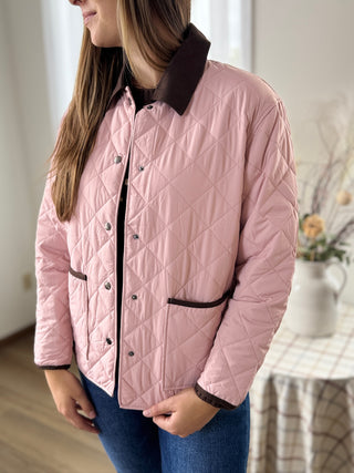 Person wearing a pink quilted jacket with brown accents indoors.