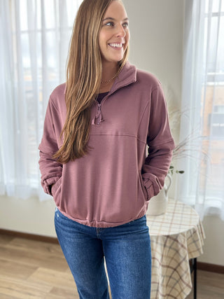 Woman wearing a pink pullover with a plaid tablecloth and curtains in the background