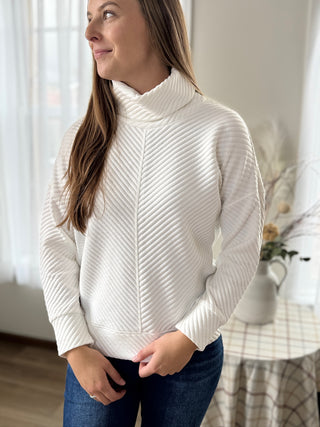 Woman wearing a white ribbed sweater in a home setting