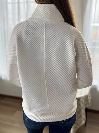 Person wearing a textured white sweater with a blurred background