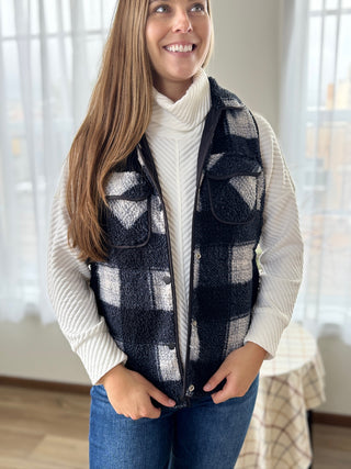 Woman wearing a plaid vest over a white sweater in a home setting