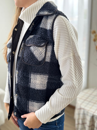 Person wearing a navy and white checkered vest over a white sweater.