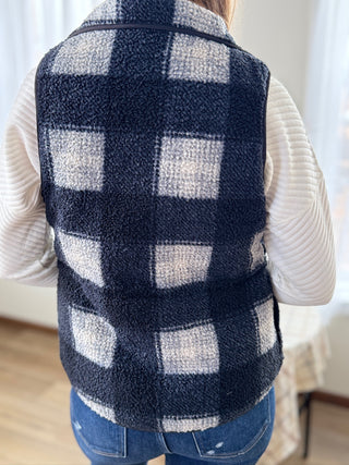 Person wearing a navy and white checkered vest over a white sweater.