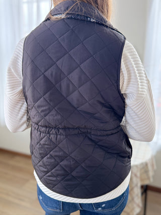 Person wearing a navy quilted vest over a white shirt with a blurred background