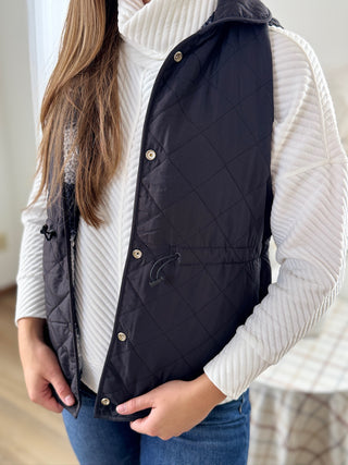 Person wearing a navy quilted vest over a white sweater