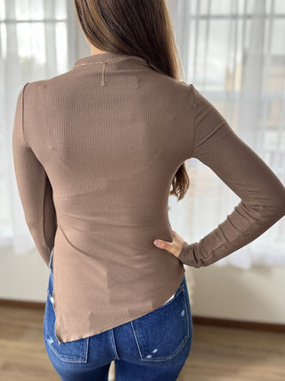 Person wearing a brown ribbed long-sleeve top and blue jeans indoors.