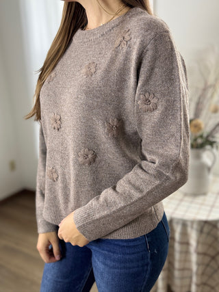 Person wearing a brown sweater with floral patterns in a room setting.
