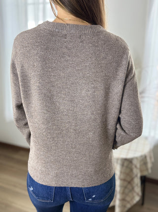 Person wearing a brown sweater and blue jeans in a room with white curtains.